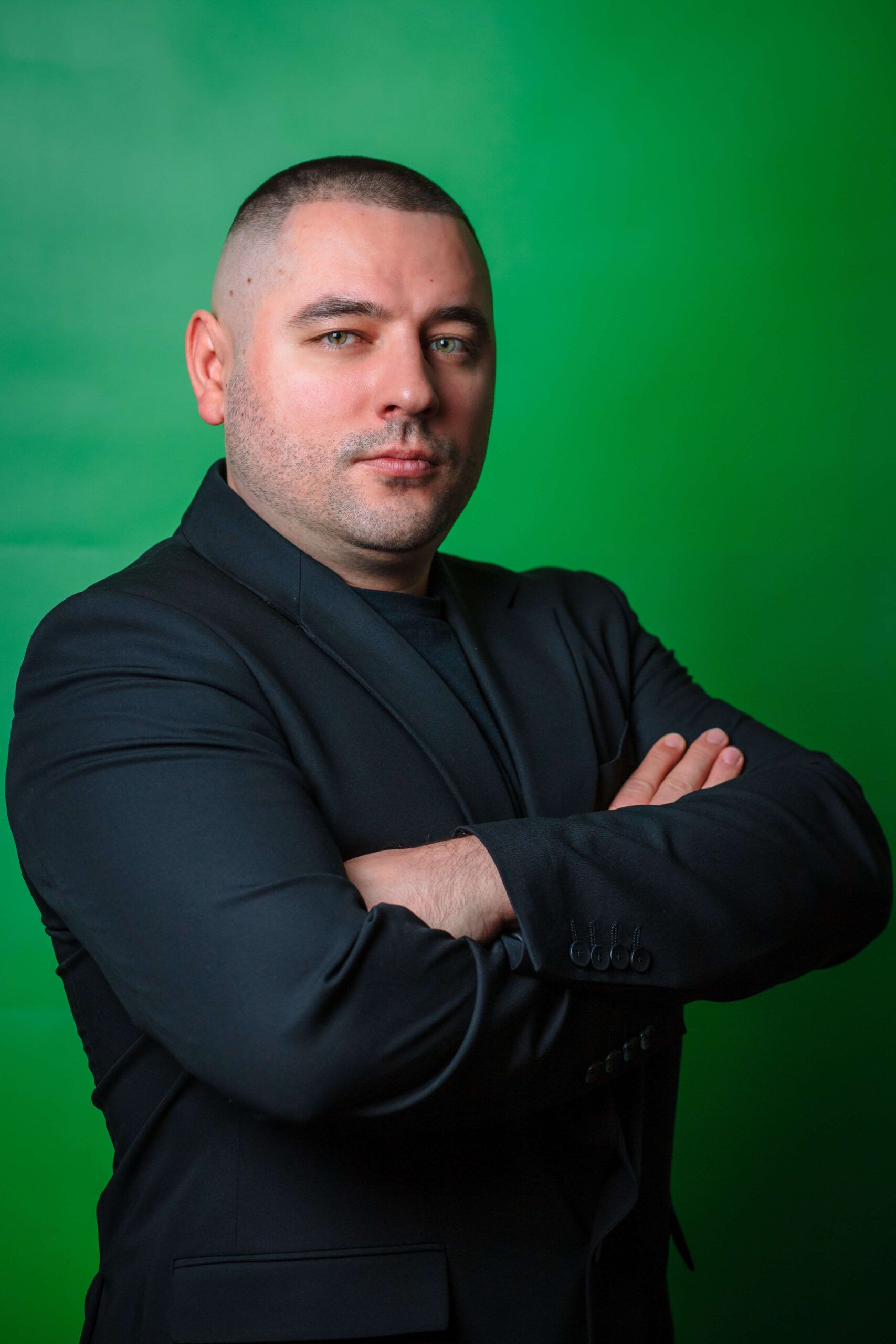 Portrait photo of the manager of Express Heroes company from Lublin, wearing dark clothes and a serious expression, standing in front of a green background.