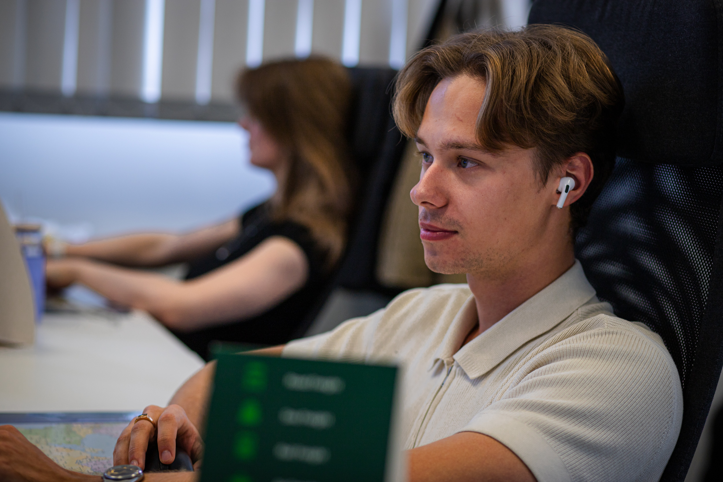 Express Heroes team member wearing a wireless earbud at his desk, with a colleague working in the background.