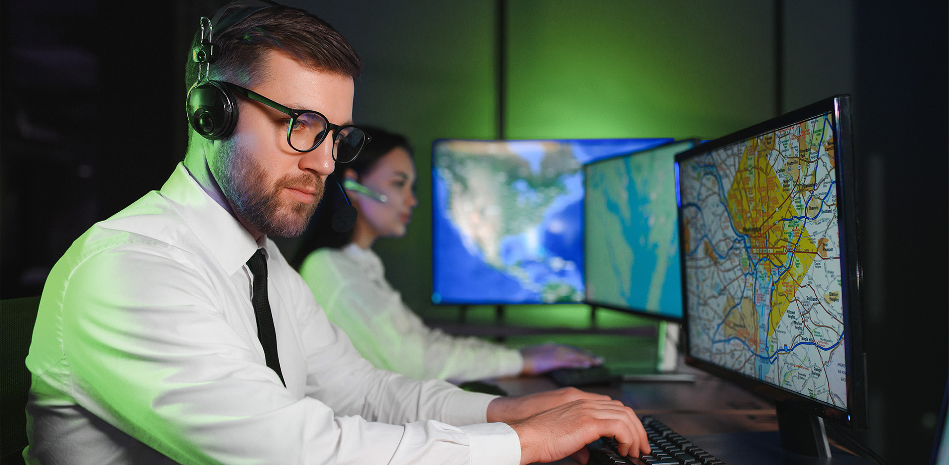 Transport coordinator wearing a headset at a workstation with maps displayed on multiple monitors.